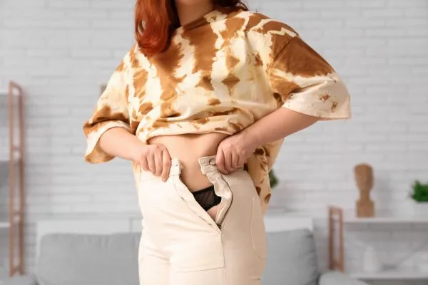 Image of woman trying to do her trousers up after pregnancy weight gain Devizes