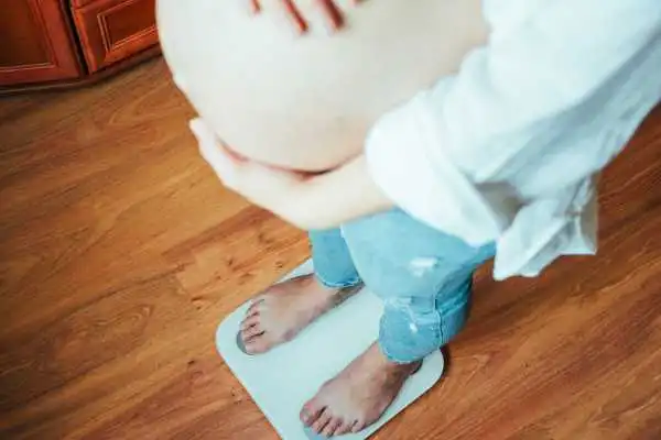 Image of woman weighing herself and experiencing weight gain through pregnancy Devizes